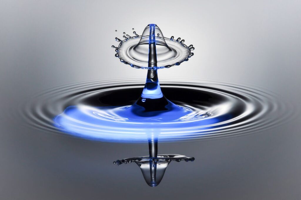 Dynamic macro photography of a water droplet splash with mirror reflection in vibrant blue tones.